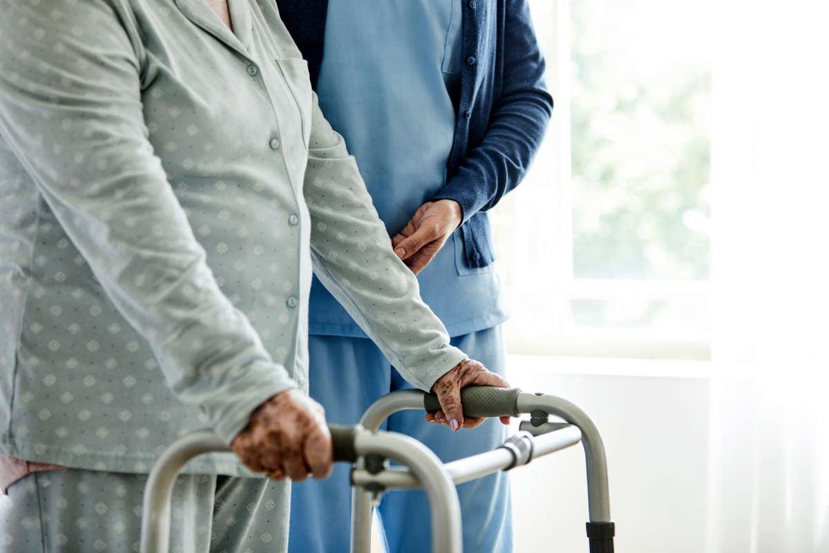 Elder care worker assisting an elderly person using a walking aid