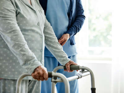 Elder care worker assisting an elderly person using a walking aid