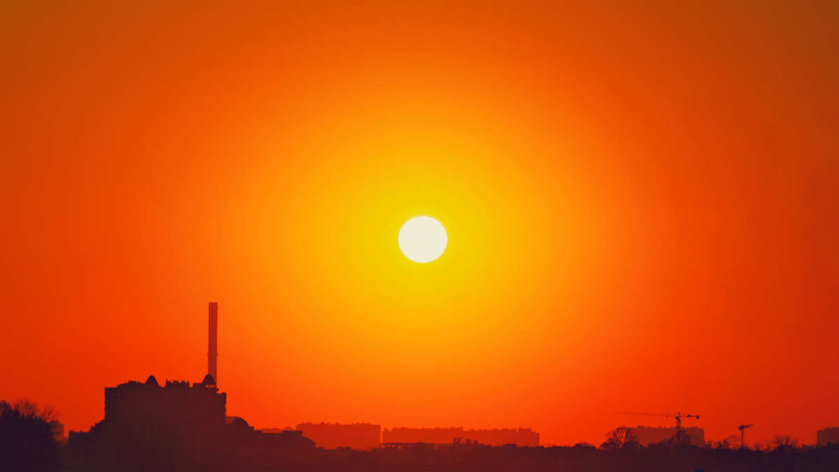 Bright sun in orange, cloudless sky over city