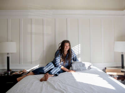 A woman smiles while sitting on her bed, in her bedroom