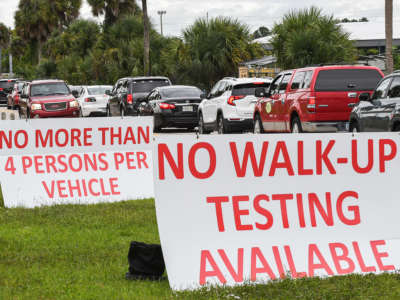 cars line up behind two signs, the foremost stating that no walk-up covid tests are available.