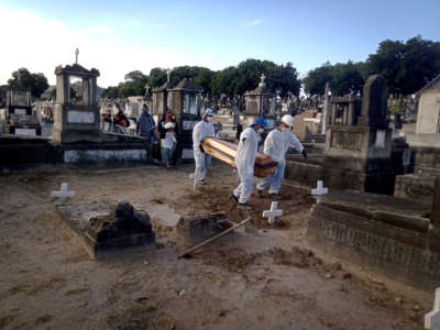 Pollbearers in PPE bring a coffin to a grave in preparation for burial