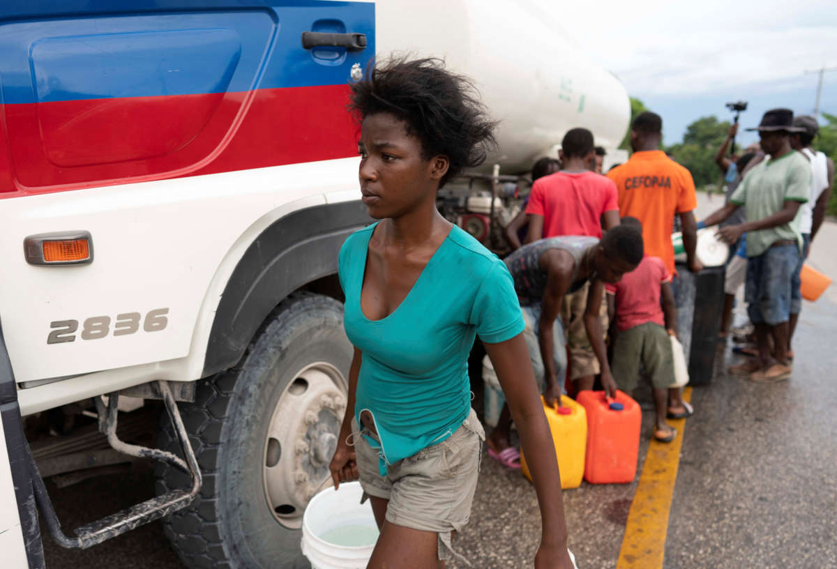 A young woman carries water away from a truck supplying it to a line of waiting people