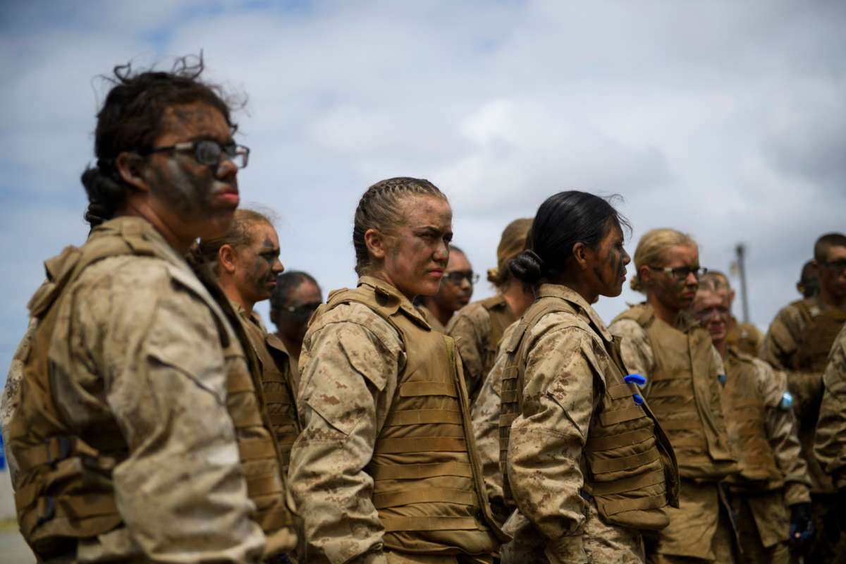 Mud-smeared female soldiers stand in a clump