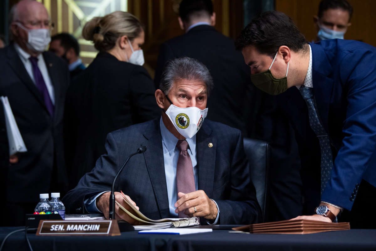 Joe Manchin looks surprised at something an aide is telling him while seated at a hearing