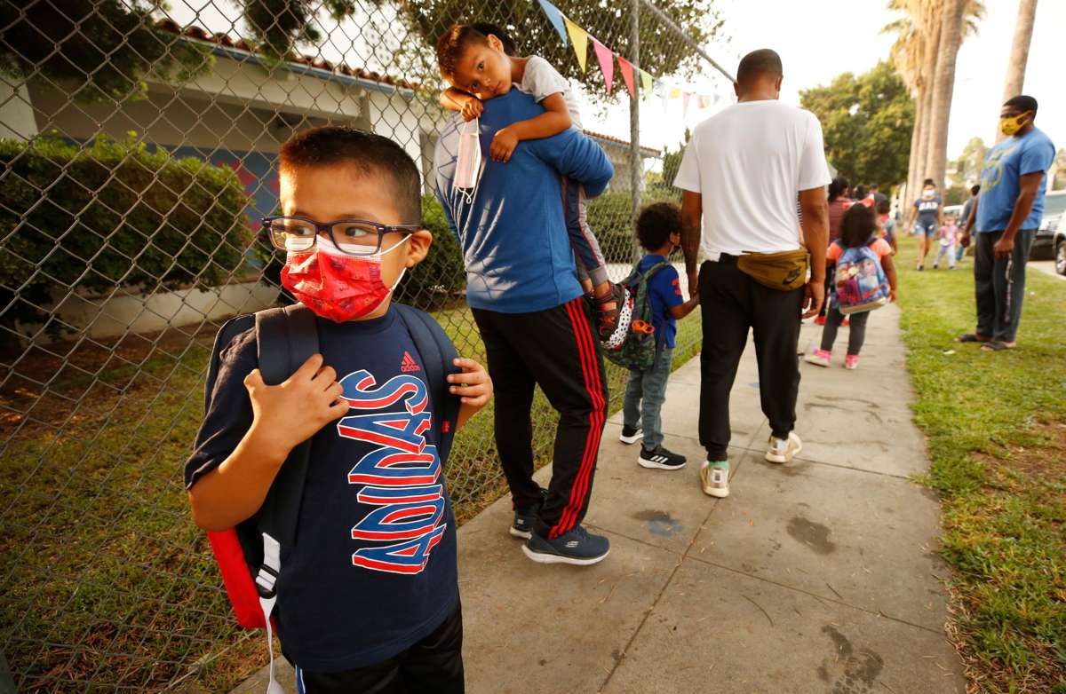 A line of children and their families wait to enter a school building