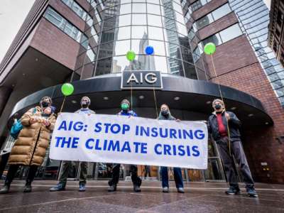 Protesters hold a sign reading "AIG: STOP INSURING THE CLIMATE CRISIS" during an outdoor protest