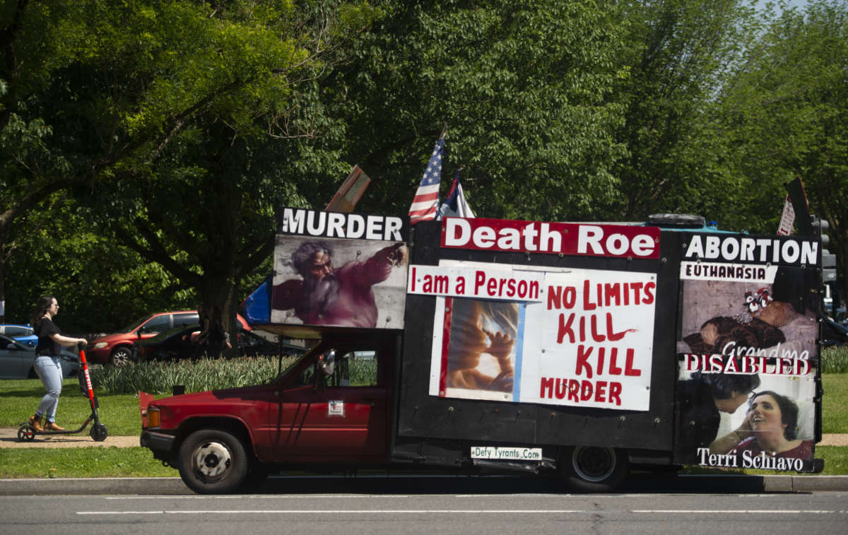 A woman rides a scooter past an anti-abortion activist's truck in Washington, D.C., on May 16, 2019.