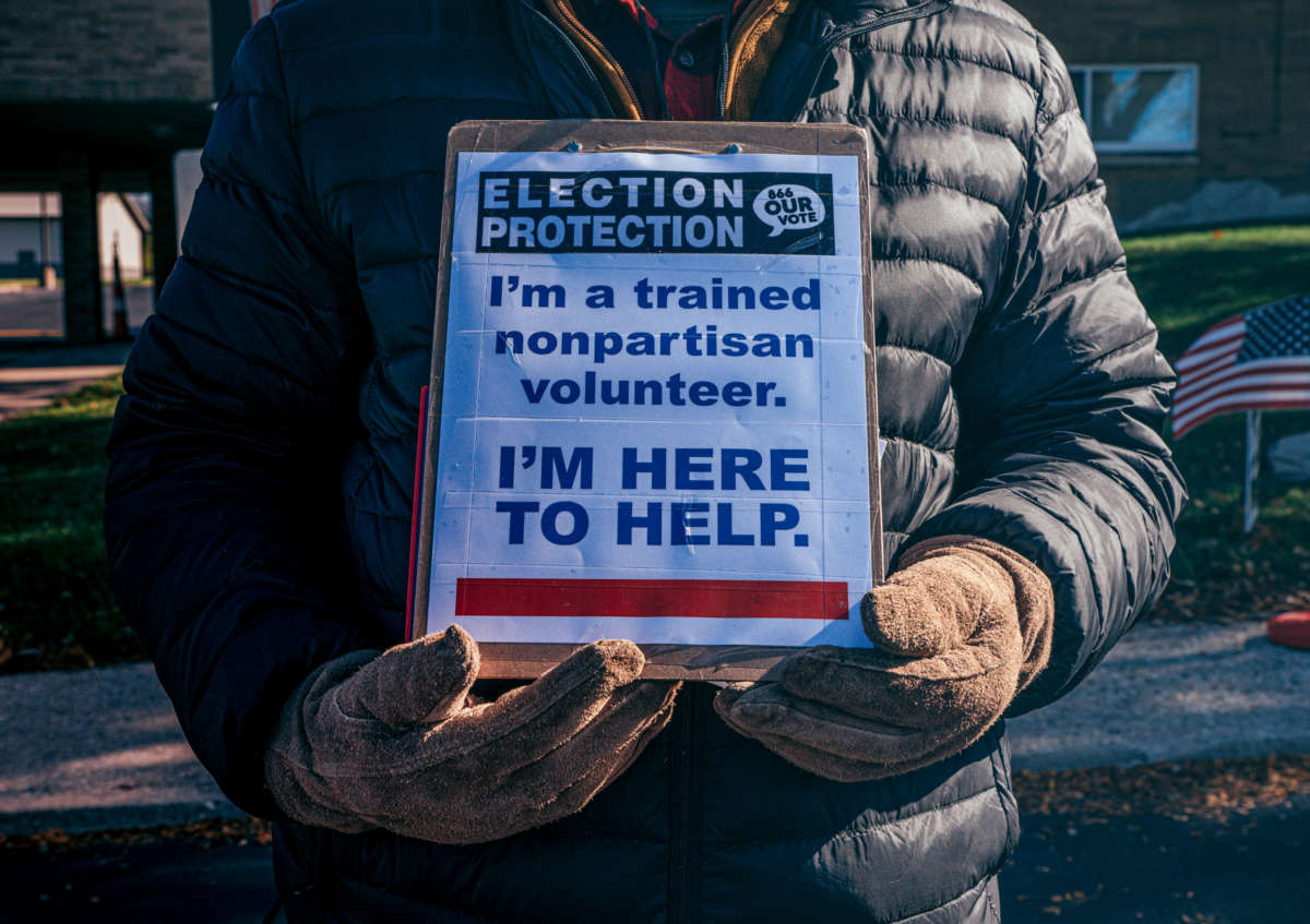 An "election protection" volunteer stands outside of a polling location at Precious Blood Church with a sign to ensure that no voter intimidation occurs on Election Day 2020 in Dayton, Ohio.