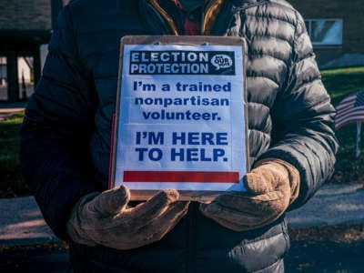 An "election protection" volunteer stands outside of a polling location at Precious Blood Church with a sign to ensure that no voter intimidation occurs on Election Day 2020 in Dayton, Ohio.