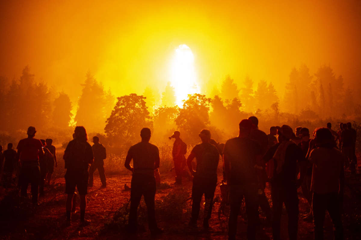 Local youth and volunteers gather in an open field and wait to support firefighters during a wildfire next to the Greek village of Kamatriades, near Istiaia, northern Evia (Euboea) island on August 9, 2021.