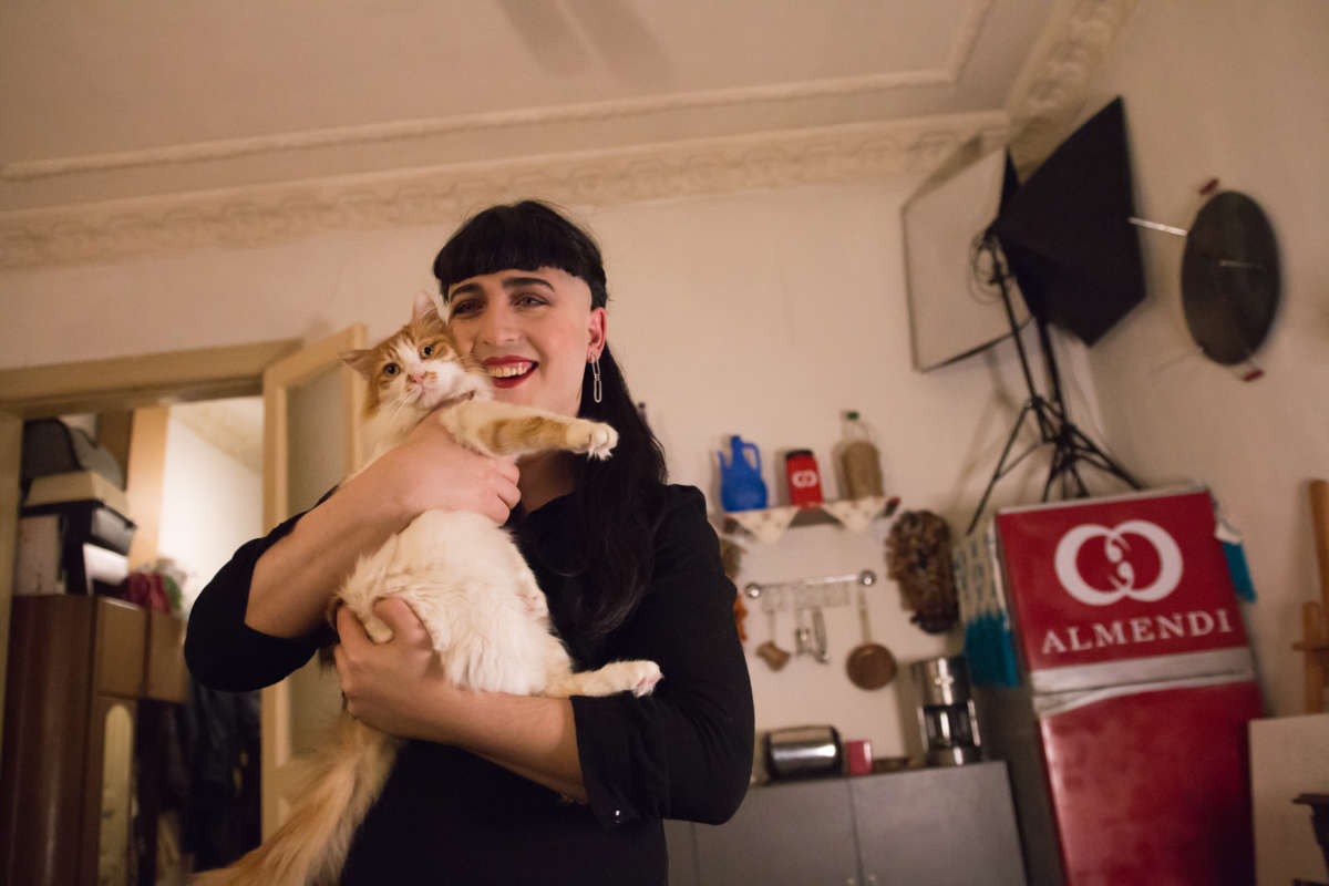 Çağlar Almendi holding their cat, Spot, in front of a set for popular YouTube videos.