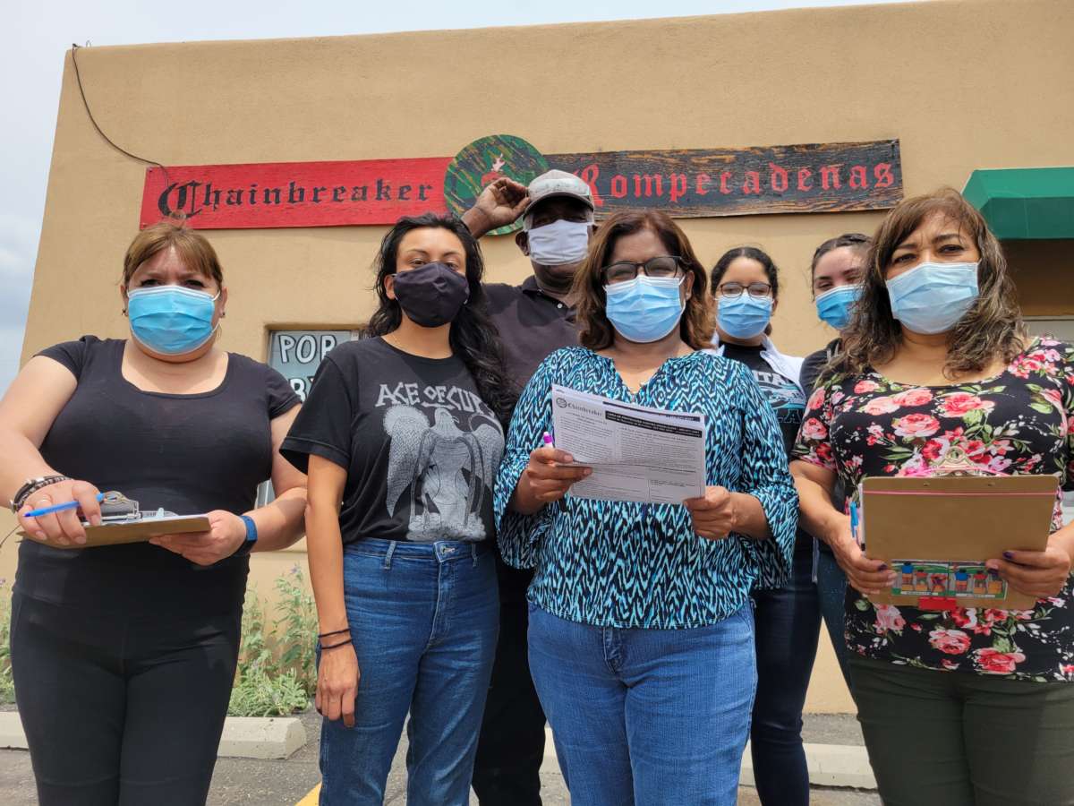 Masked people stand together for a photo in front of a building with a sign reading "Chainbreakers Romperadenas"