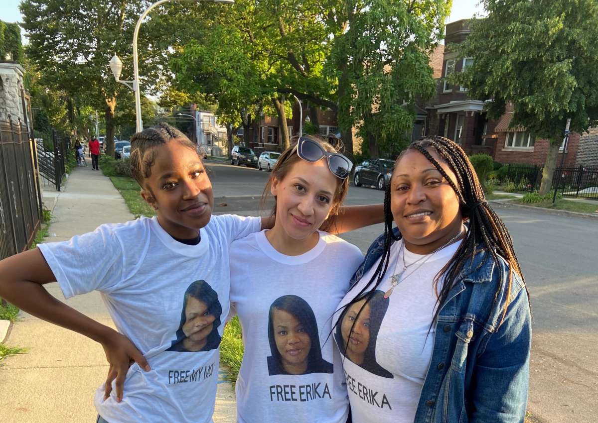 Three women pose for a photo while wearing matching shirts, each bearing Erika Ray's face with the message "FREE ERIKA" written below it.