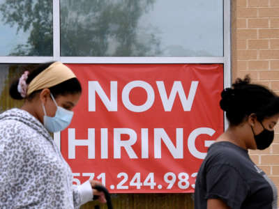 People walk by a "NOW HIRING" sign