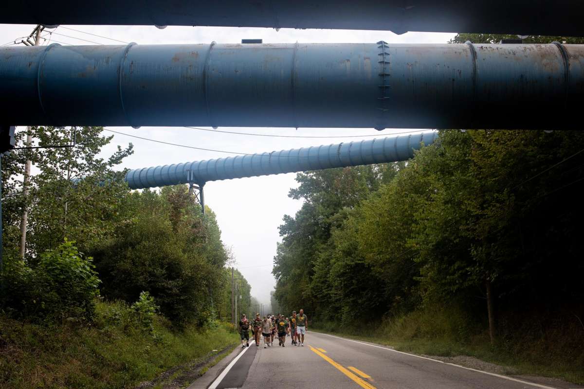 People march down an empty highway beneath what looks to be large pipelines