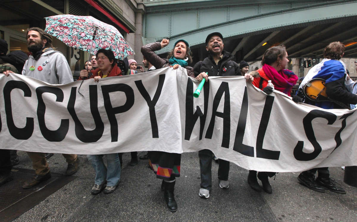 Protesters march behind a banner reading "OCCUPY WALL STREET" during an outdoor, pre-covid protest