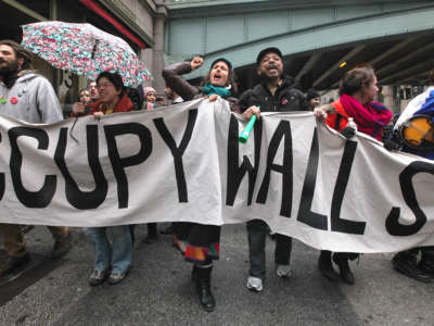 Protesters march behind a banner reading "OCCUPY WALL STREET" during an outdoor, pre-covid protest