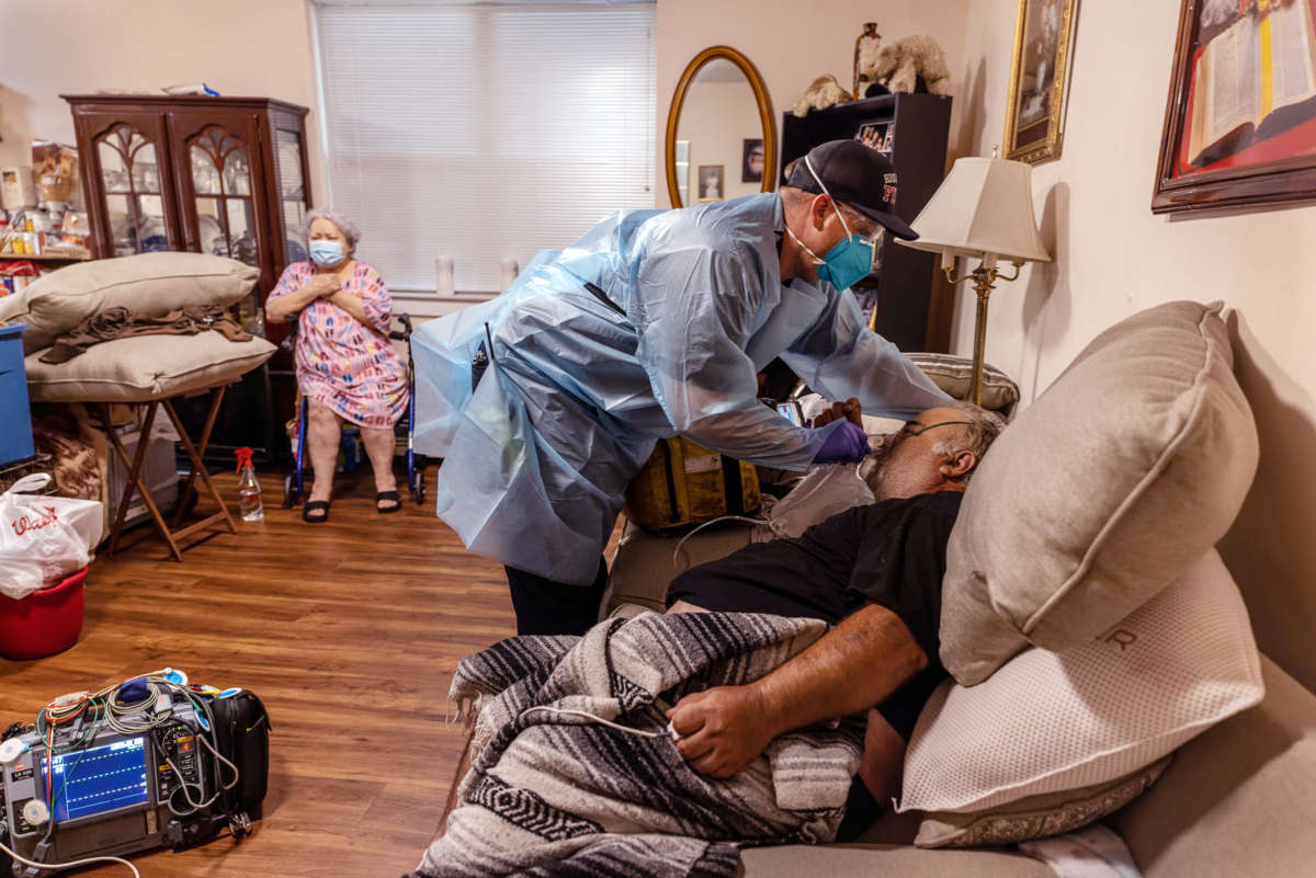 A man recieves medical care in his home while a woman in the background looks concerned