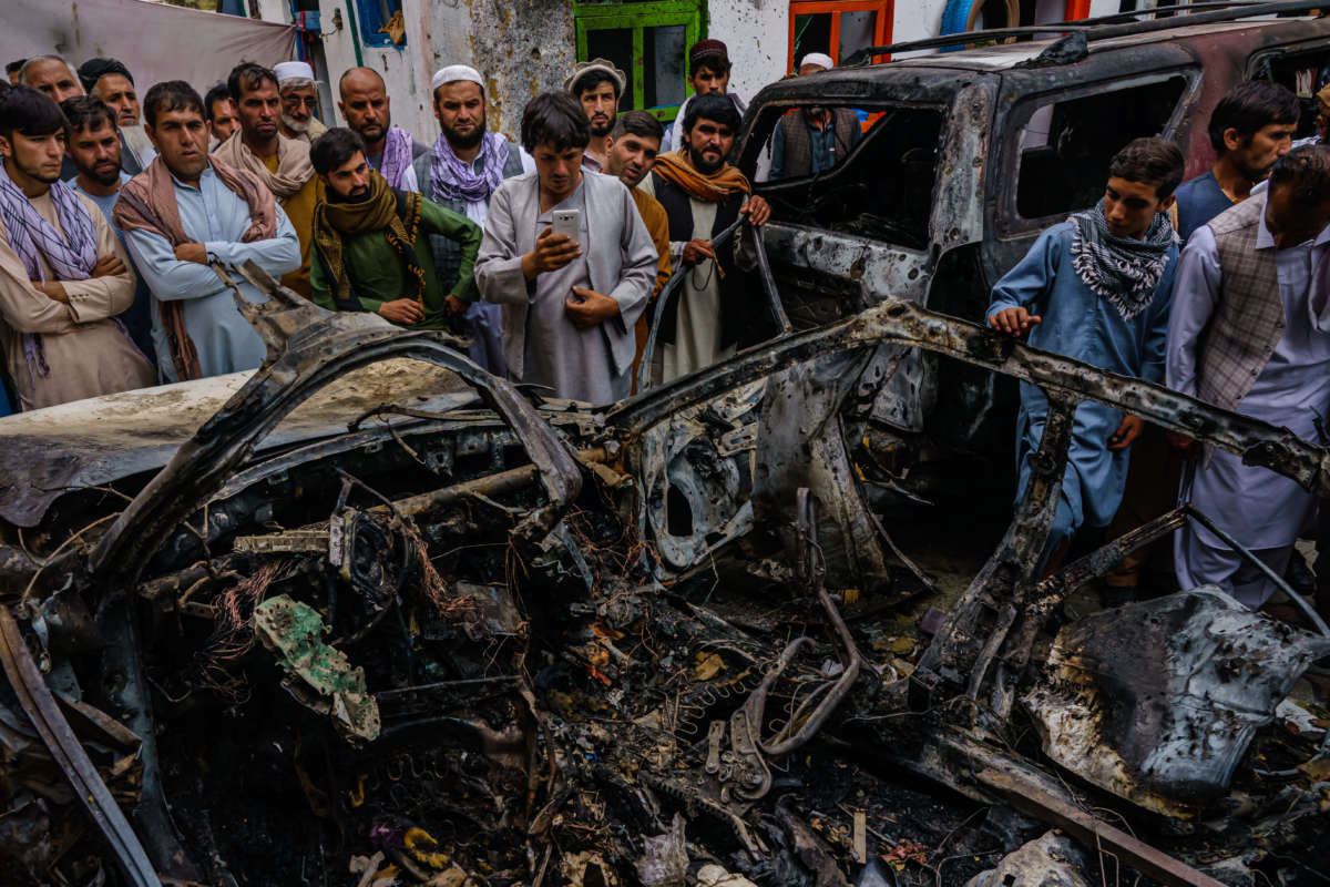 Relatives and neighbors of the Ahmadi family gathered around the incinerated husk of a vehicle targeted and hit earlier Sunday afternoon by a U.S. drone strike, in Kabul, Afghanistan, on August 30, 2021.