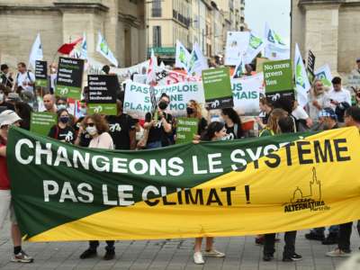 Protesters hold a banner reading "Change the system not the climate" while demanding action against climate change on the sidelines of the International Union for Conservation of Nature (IUCN) congress in Marseille, France, on September 3, 2021.