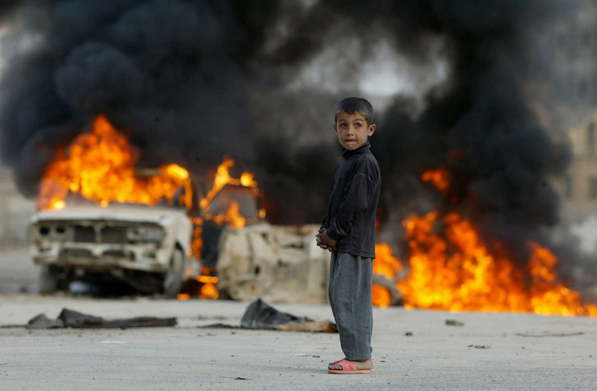 A young Iraqi boy stands in front of burning vehicles in Baghdad, Iraq, Sunday, April 13, 2003.