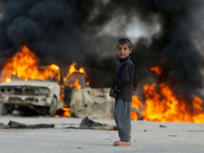 A young Iraqi boy stands in front of burning vehicles in Baghdad, Iraq, Sunday, April 13, 2003.