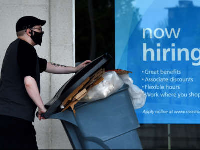 A man wearing a face mask walks past a sign "Now Hiring" in front of a store on May 14, 2020, in Arlington, Virginia.