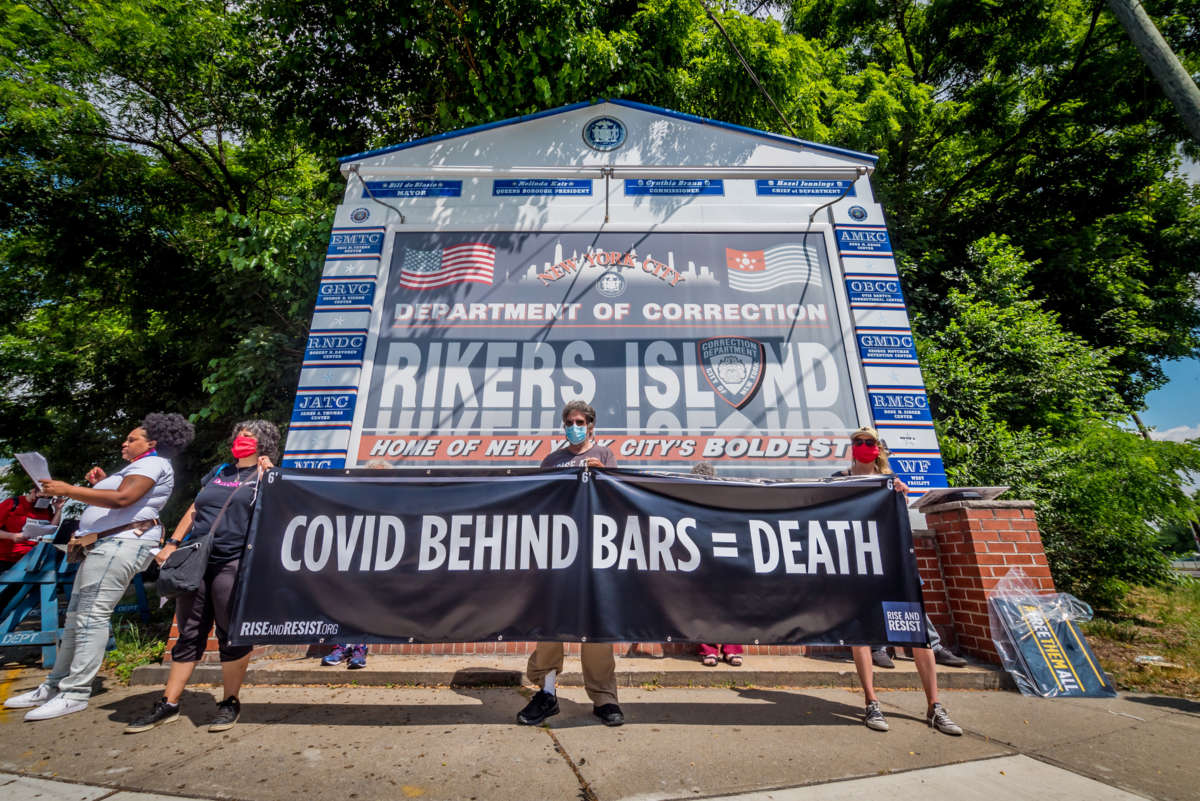 People display a sign reading "COVID BEHIND BARS = DEATH" during an outdoor protest