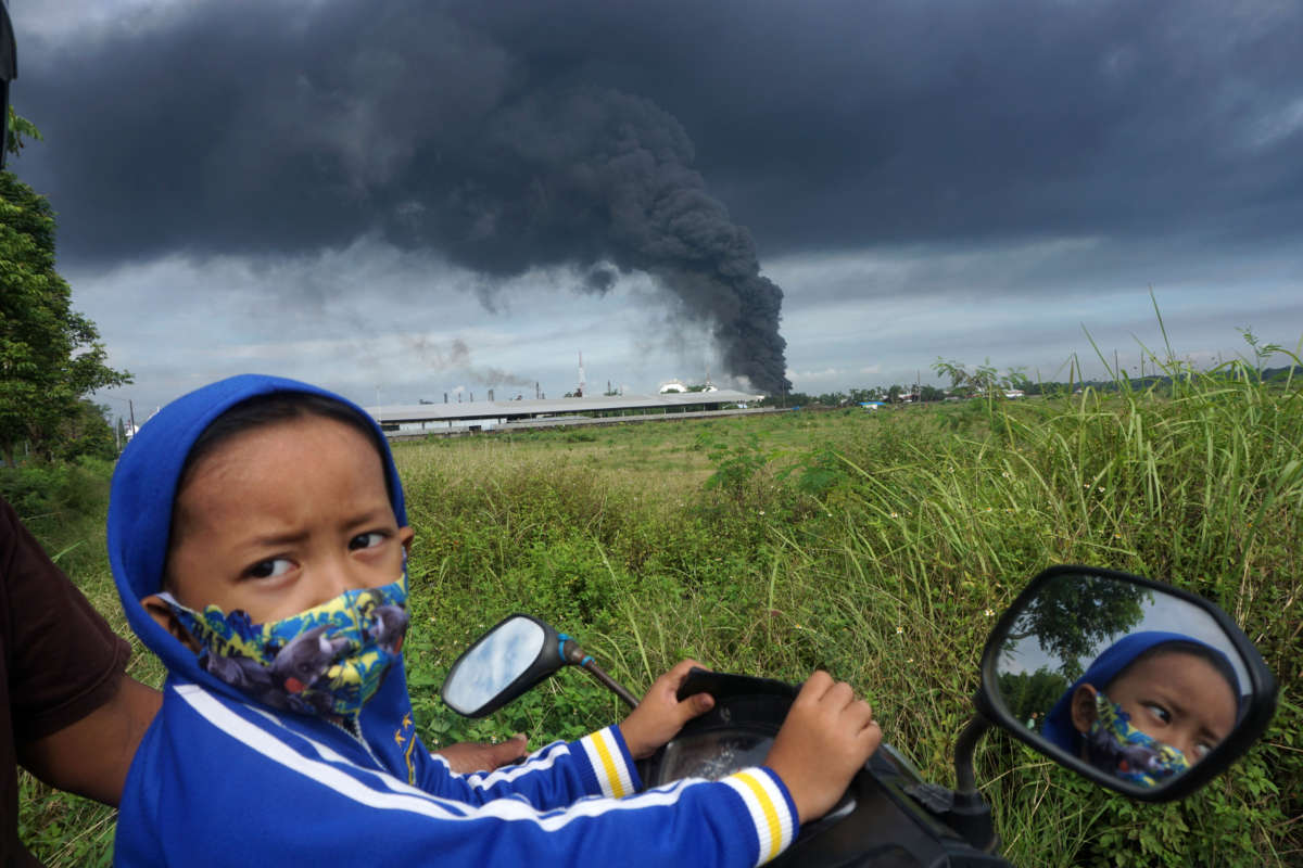 A boy sits on a motorbike as a smoke rises from a fire in the background