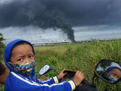 A boy sits on a motorbike as a smoke rises from a fire in the background