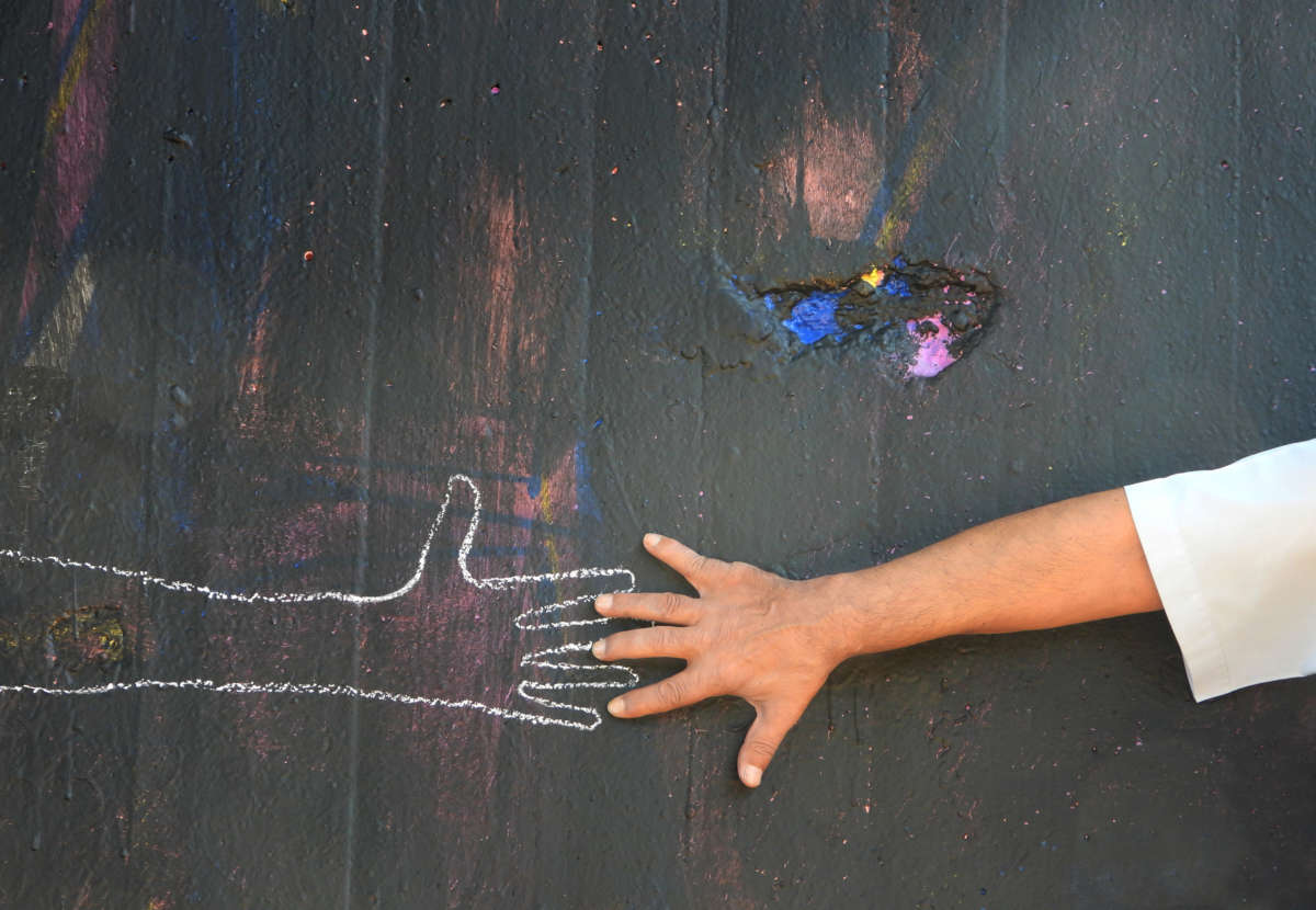 A hand reaches out to a chalk drawing of another hand