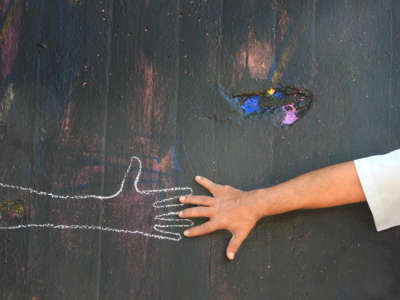 A hand reaches out to a chalk drawing of another hand