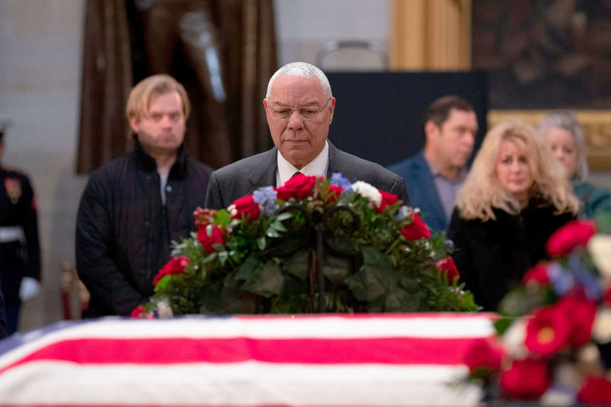 Colin Powell looks at a flag-draped coffin