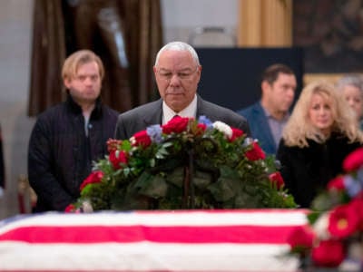 Colin Powell looks at a flag-draped coffin