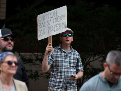 A man holds a sign reading "CRITICAL RACIST THEORY IS POISON" during a protest