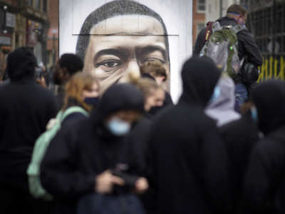 A mural of George Floyd peers over the heads of people walking on the sidewalk