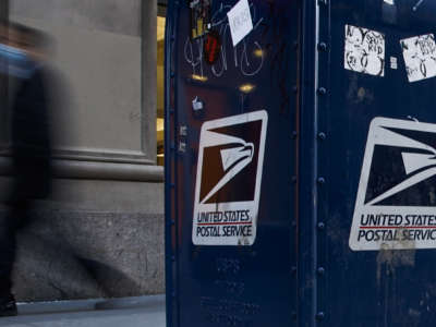 A USPS Postal box stands on a city corner