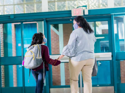 A mother and young student wear masks while leaving school