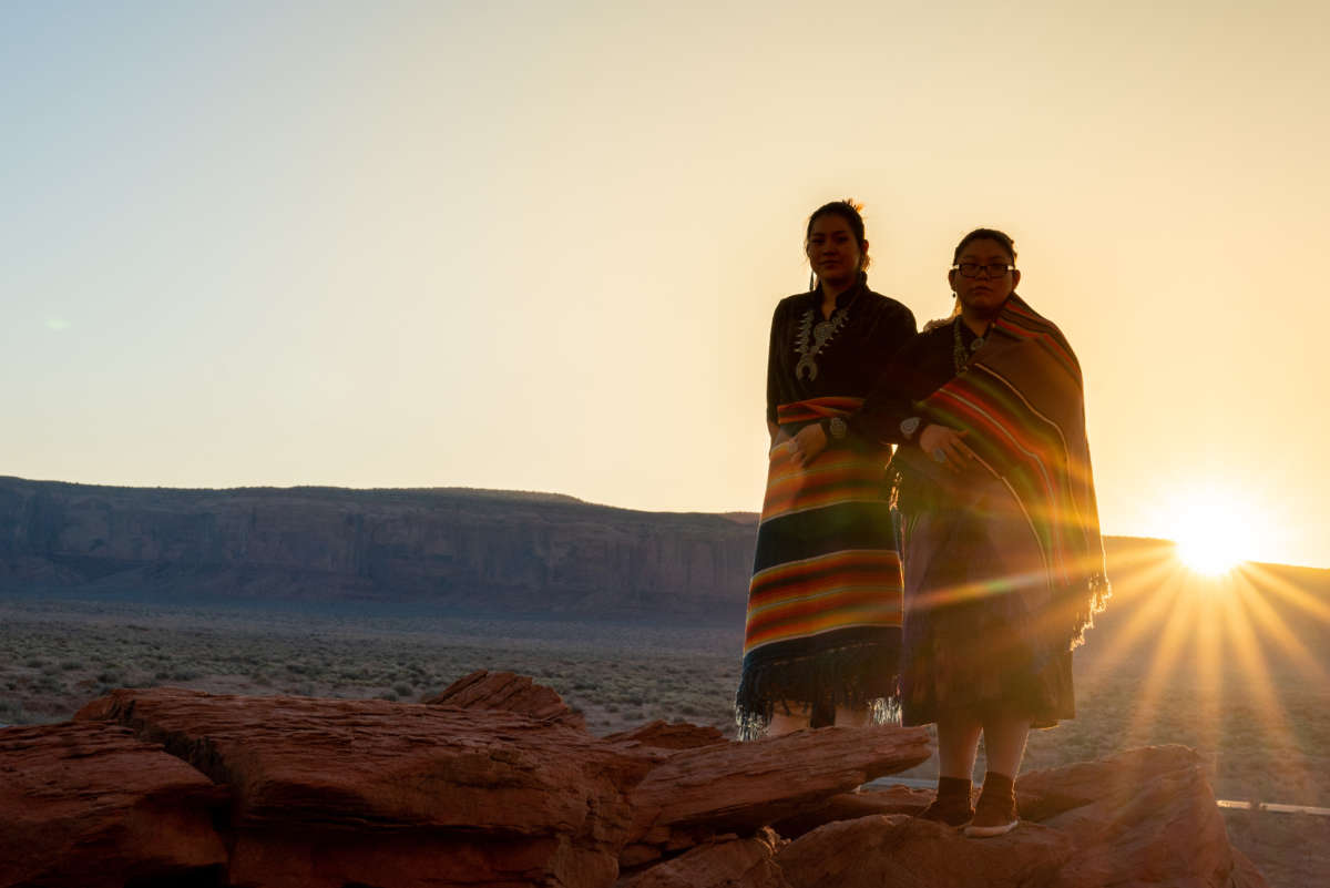 Two Teenage Native American Indigenous Navajo Sister in Traditional Clothing Enjoying the Vast Desert and Red Rock Landscape in the Famous Navajo Tribal Park in Monument Valley Arizona at Dawn