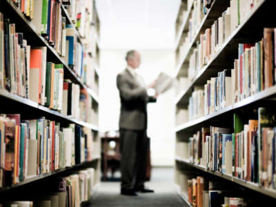 Man in suit looks at book in library shelves
