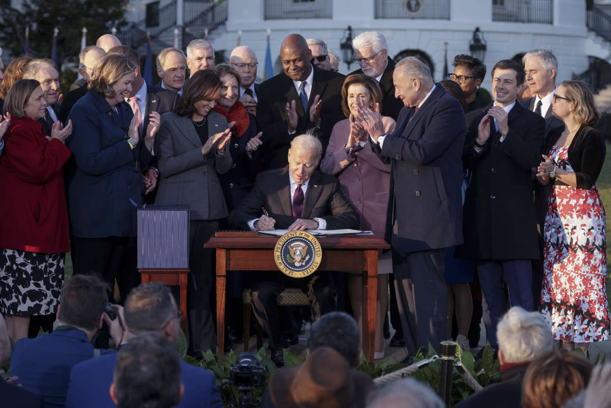 Joseph Robinette Biden signs a bill into law while others cheer him on