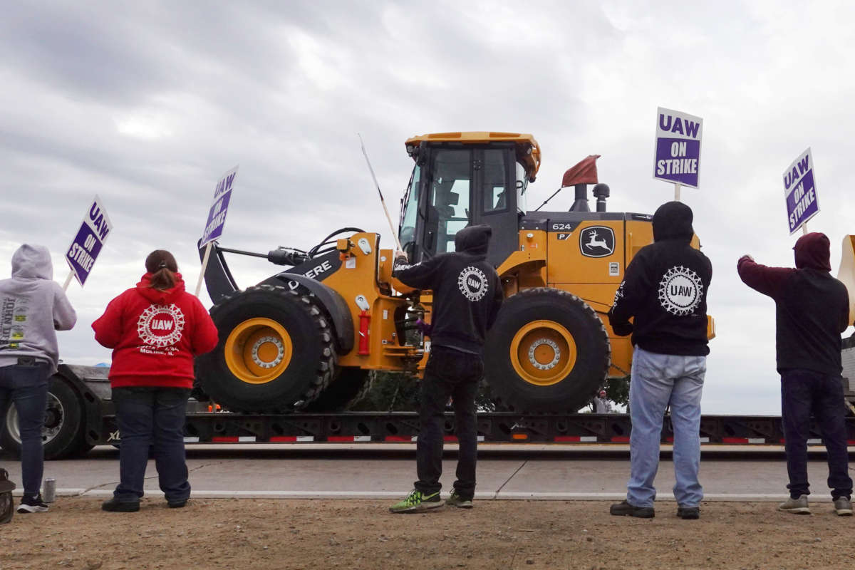 At truck hauls a piece of John Deere equipment from the factory past workers picketing outside of the John Deere Davenport Works facility on October 15, 2021, in Davenport, Iowa.