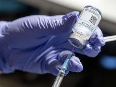 A nurse draws a COVID-19 vaccine from an ampoule into a syringe.