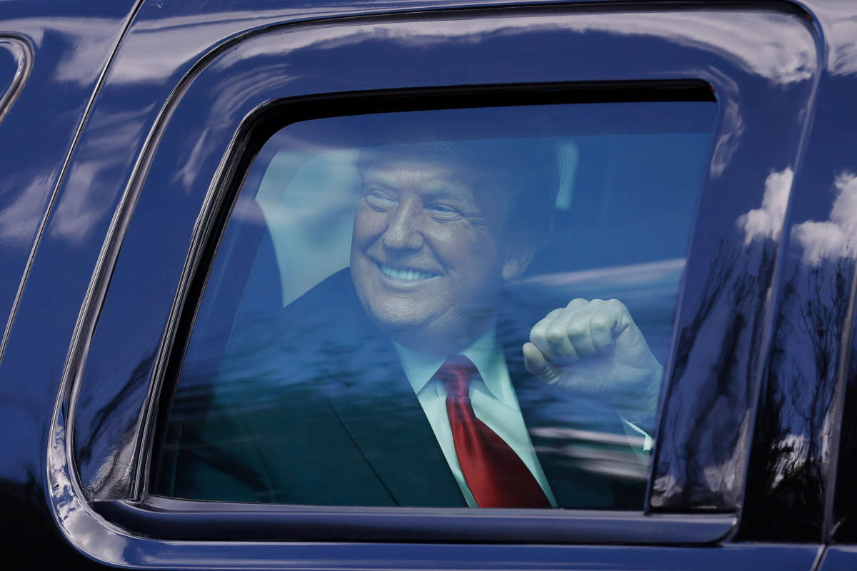 Donald Trump smiles and holds up a fist from the inside of a vehicle