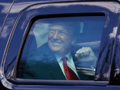 Donald Trump smiles and holds up a fist from the inside of a vehicle