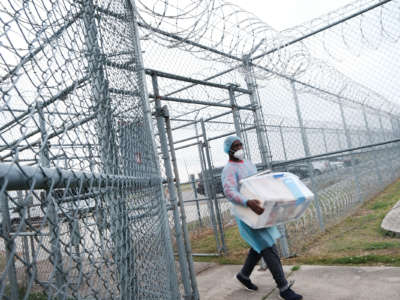 A medical worker walks a cooler of supplies through barbed wire gates and into a prison