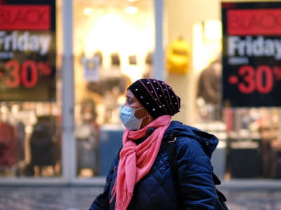 A woman in a mask and cold weather clothes walks past mall sineage