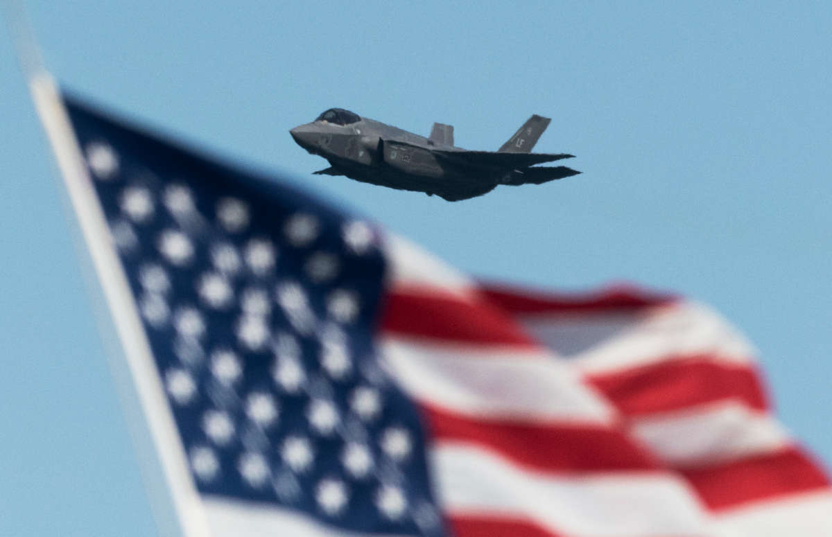 An F-35 fighter jet flies over a US flag