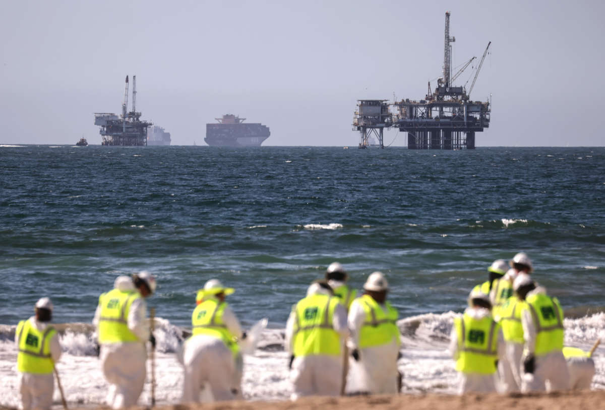 Cleanup workers search for contaminated sand and seaweed in front of drilling platforms and container ships about one week after an oil spill from an offshore oil platform on October 9, 2021, in Huntington Beach, California.